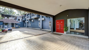 Un bâtiment avec une porte rouge, un espace de stationnement couvert et un escalier menant à un étage supérieur.