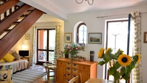A cozy room with a wooden staircase, a dining area with a wooden table, and a bed with floral bedding. - Maison sur les hauteurs de Collioure, avec vue panoramique (Collioure)