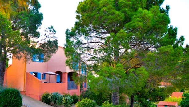 A building with a red exterior, surrounded by lush greenery and trees. - Maison sur les hauteurs de Collioure, avec vue panoramique (Collioure)