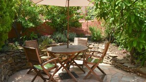 A patio with a round table and four wooden chairs, an umbrella, and surrounding greenery. - Maison sur les hauteurs de Collioure, avec vue panoramique (Collioure)