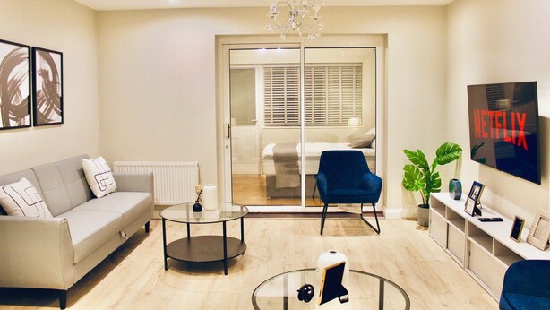 Un soggiorno moderno con un divano, una poltrona blu, un tavolino in vetro e una TV a parete.