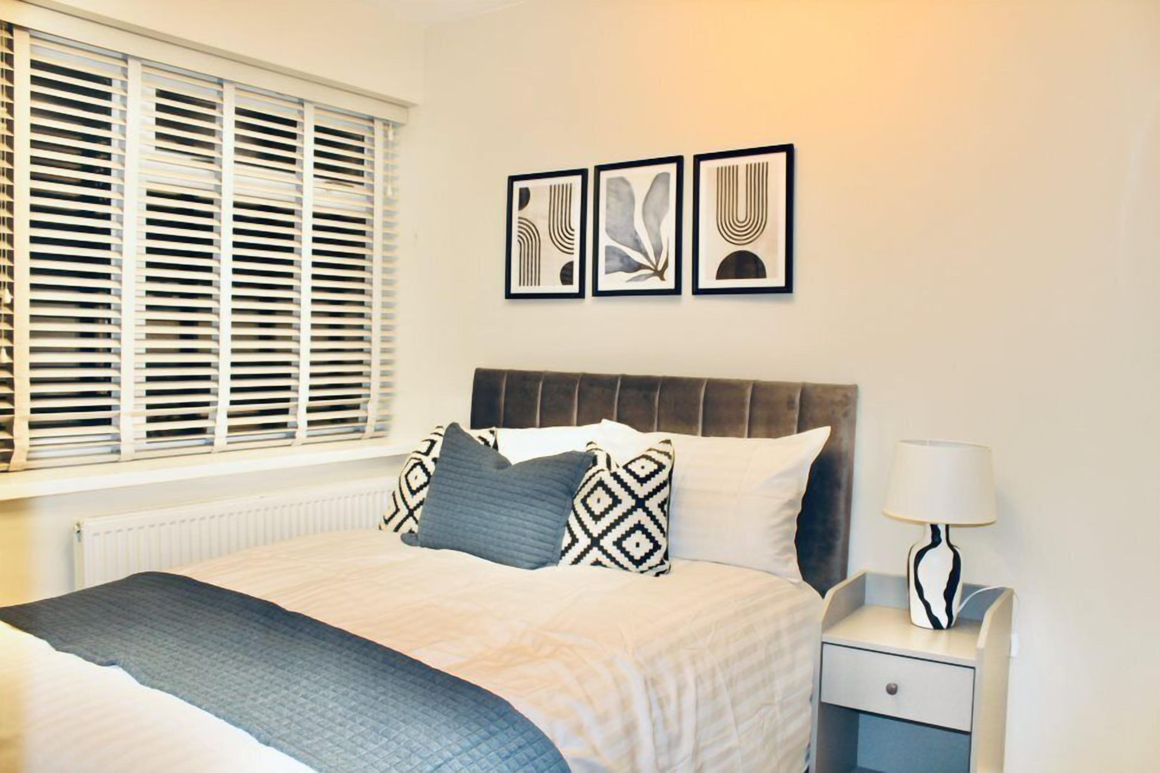 A neatly made bed with patterned pillows, a bedside table with a lamp, and three framed artworks on the wall.