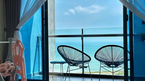 A room with a large window, two black chairs, and a pink chair. - Atlantis Residence 2 (Malacca City)