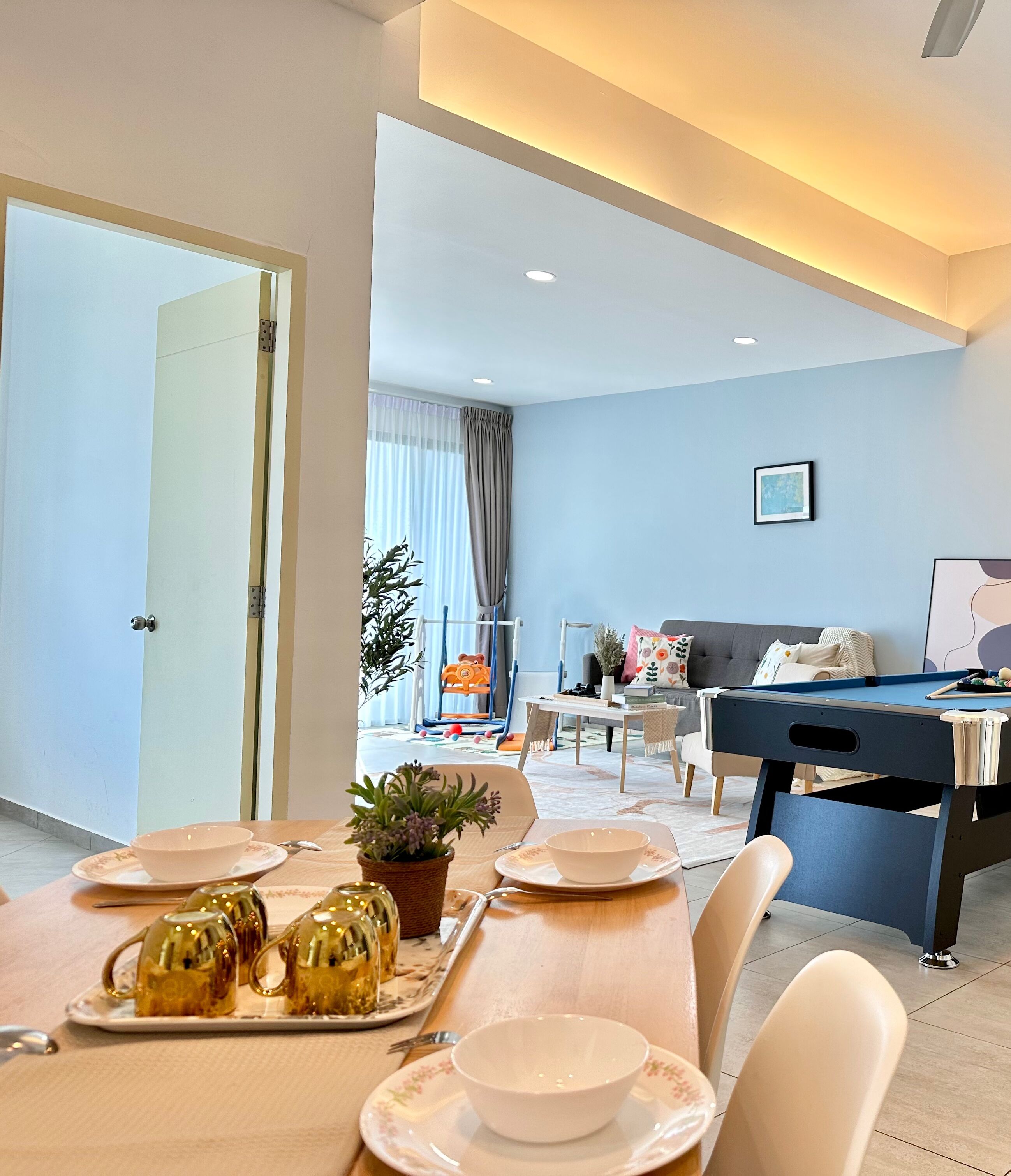 A modern living room with a pool table, dining area with a table set for two, and a sofa.