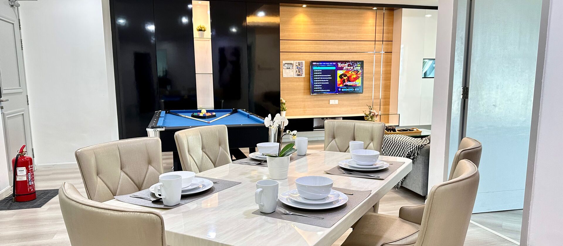 A dining area with a pool table, beige chairs, and a table set for four with white tableware.