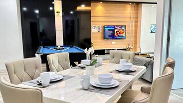 A dining area with a pool table, beige chairs, and a table set for four with white tableware.