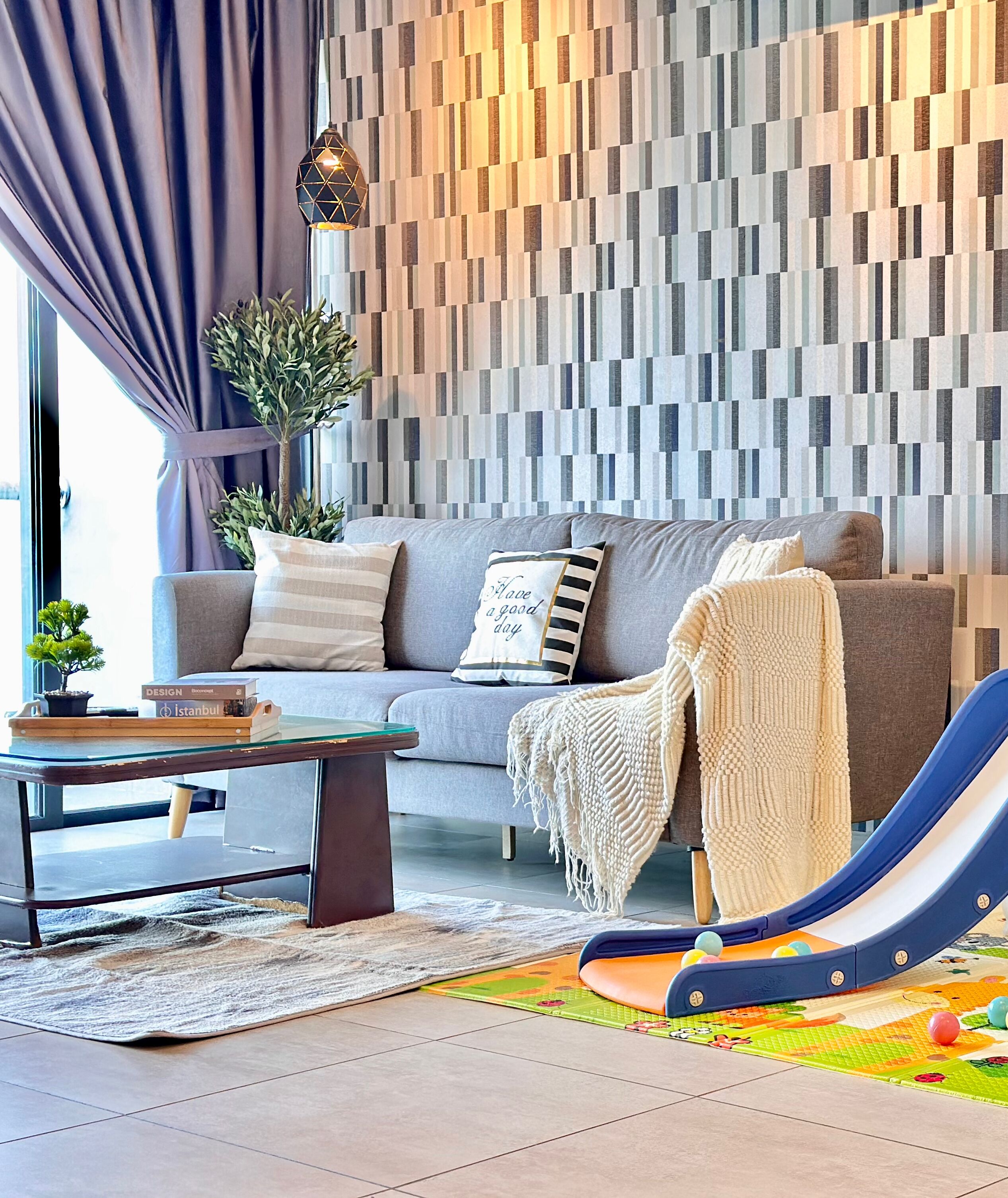 A living room with a grey sofa, a glass coffee table, a patterned wall, a plant, and a children's slide.