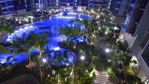 A nighttime view of a hotel with a central swimming pool surrounded by palm trees and illuminated by artificial lights. - Atlantis Residence 2 (Malacca City)