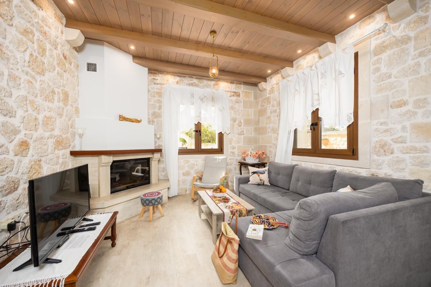 Ein gemütliches Wohnzimmer mit Steinwand, Kamin, grauem Sofa und Fernseher.