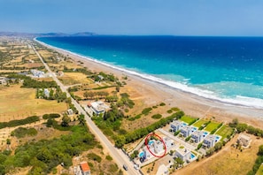 Vue aérienne d’une zone côtière comprenant une plage, une route et un complexe résidentiel composé de plusieurs bâtiments et d’une piscine.