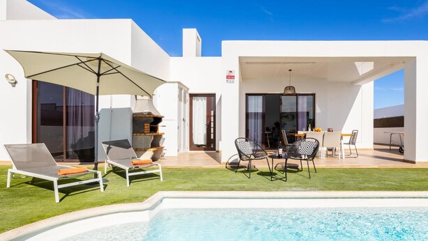 A modern outdoor pool area with lounge chairs, a barbecue, and a dining setup. - Villa Cindy - Three Bedroom Villa, Sleeps 6 (Playa Blanca)
