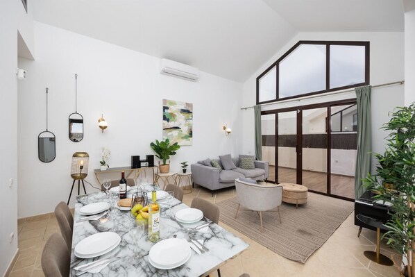 Ein moderner Essbereich mit einem Marmortisch, gedeckt für vier Personen, einer grauen Couch und einem Balkon mit Aussicht.