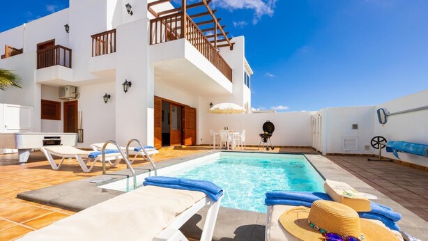 Un espace moderne aménagé au bord de la piscine, avec des chaises longues, un barbecue et un escalier menant à un niveau supérieur.