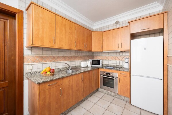 A kitchen with wooden cabinets, a granite countertop, a microwave, a coffee maker, and a refrigerator. - Villa Florencia - Two Bedroom Villa, Sleeps 4 (Puerto del Carmen)
