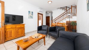 Un salon comprenant un meuble en bois, un téléviseur, un canapé, une table basse et un escalier.