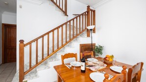 Un coin repas agrémenté d’un escalier en bois, de marches en marbre et d’une table mise pour deux, avec assiettes, verres et une bouteille de vin.