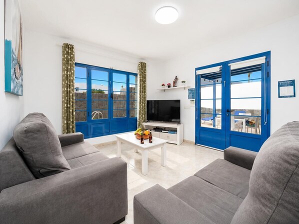 A modern living room with grey sofas, a flat-screen TV, and a coffee table with fruit and a bottle.