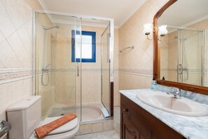 A bathroom with a glass-enclosed shower, a white toilet, a marble sink, and a wooden vanity.