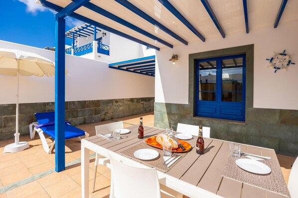 An outdoor dining area with a table set for two, a blue door, and a view of the sea.