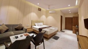 A modern hotel room with a bed, sofa, and a small dining area. - PARTH KING BEACH RESORT (Kanthi)