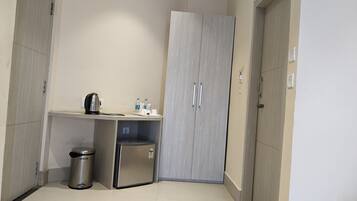 Una kitchenette compacta con cafetera, un cubo de basura y un refrigerador pequeño.