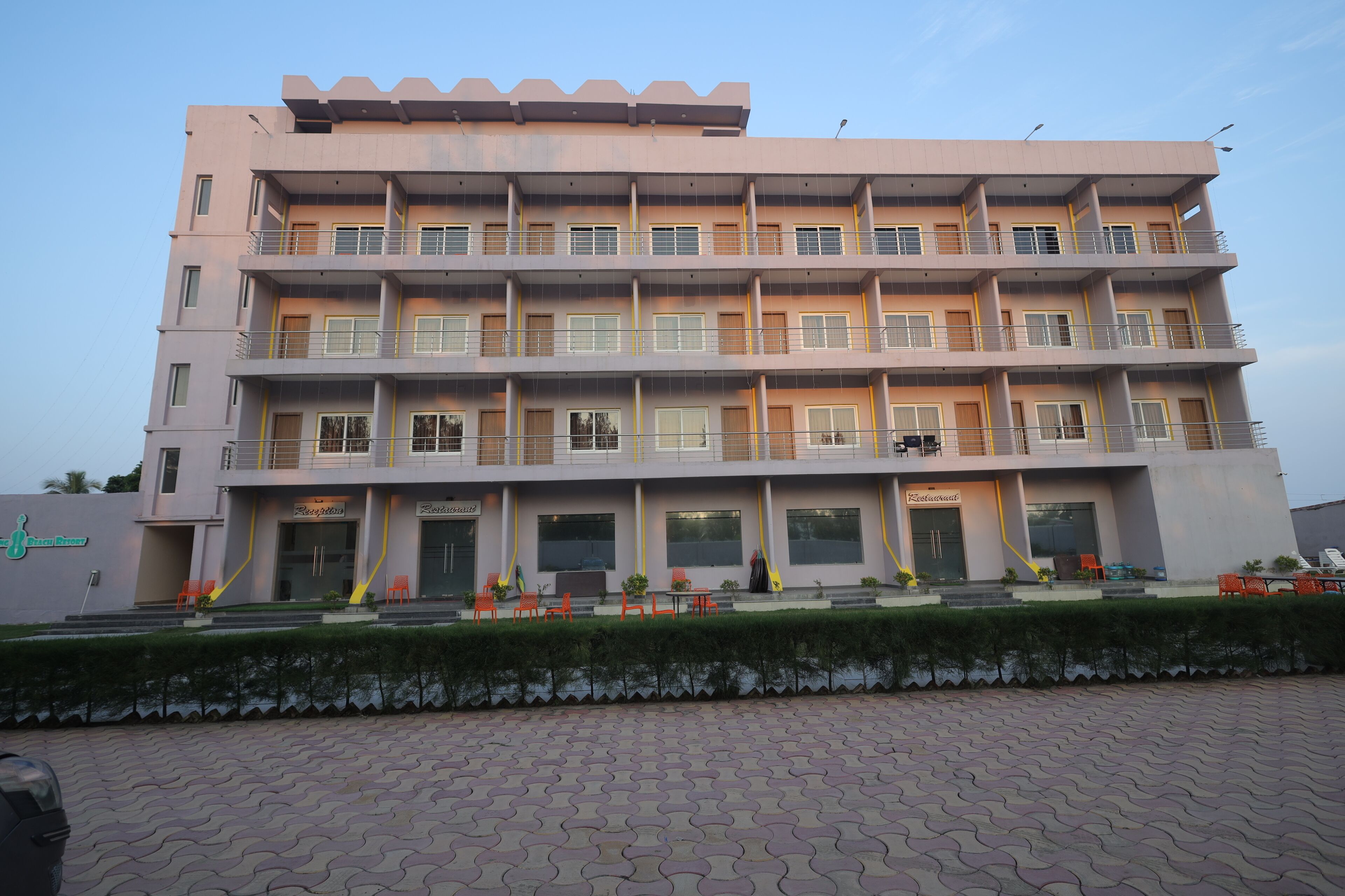 A multi-story building with a flat facade, balconies, and a paved entrance area with outdoor seating.