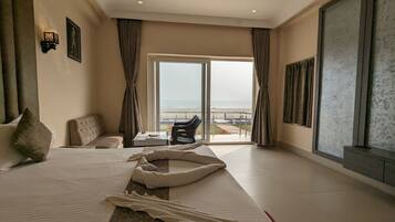 Habitación de hotel con una cama grande, un sofá, una mesita y vistas a la playa desde la ventana.