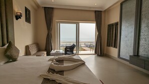 A hotel room with a large bed, a sofa, a small table, and a view of the beach through the window. - PARTH KING BEACH RESORT (Kanthi)