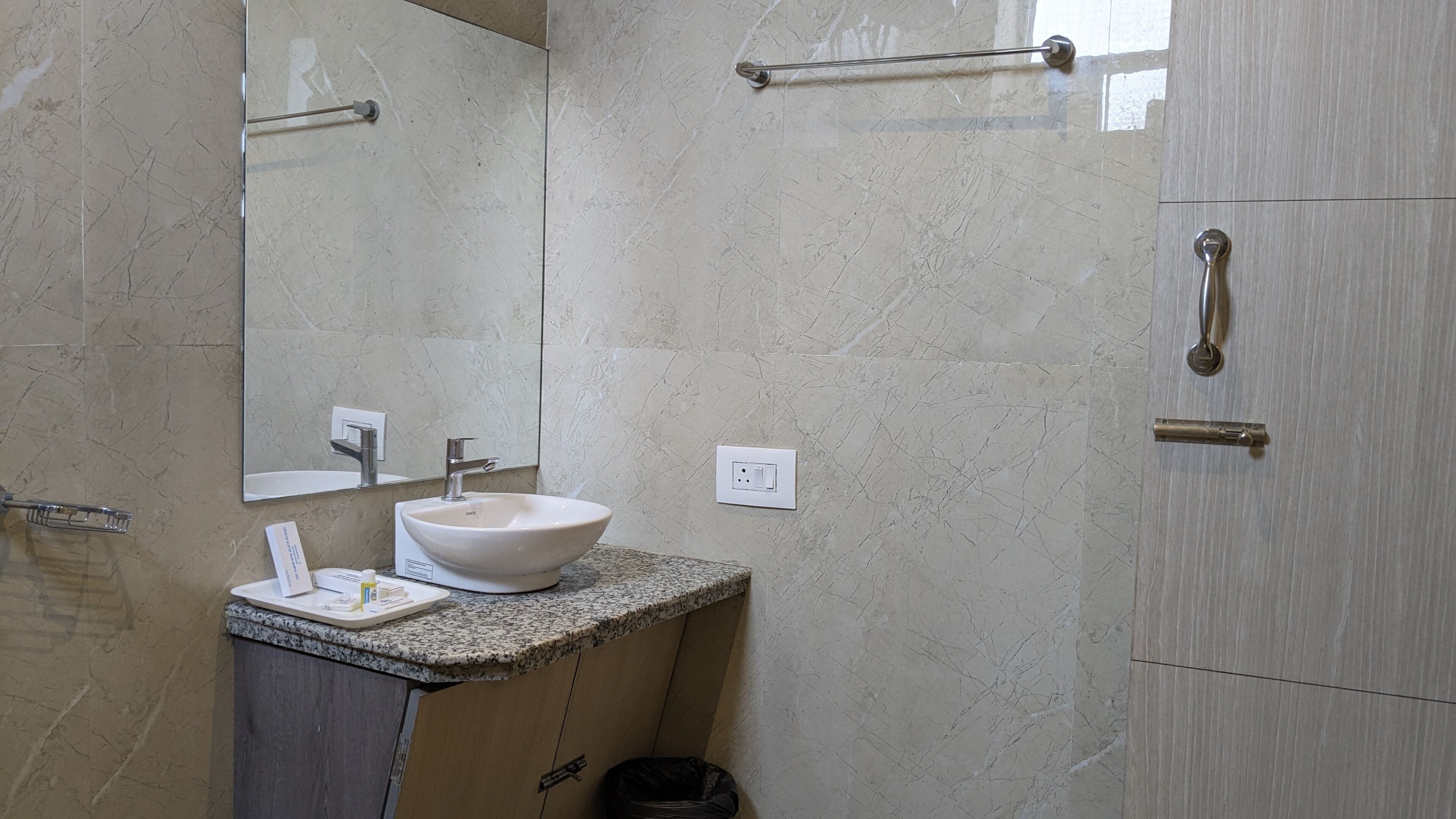 Un baño con lavamanos de mármol, espejo, toallero, puerta de ducha y un cesto de basura.