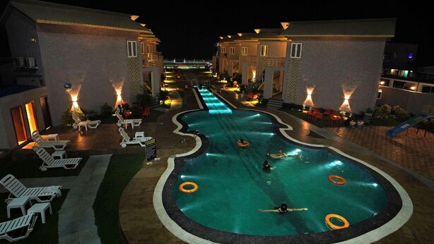 A swimming pool area at night with lounge chairs and a poolside bar. - PARTH KING BEACH RESORT (Kanthi)