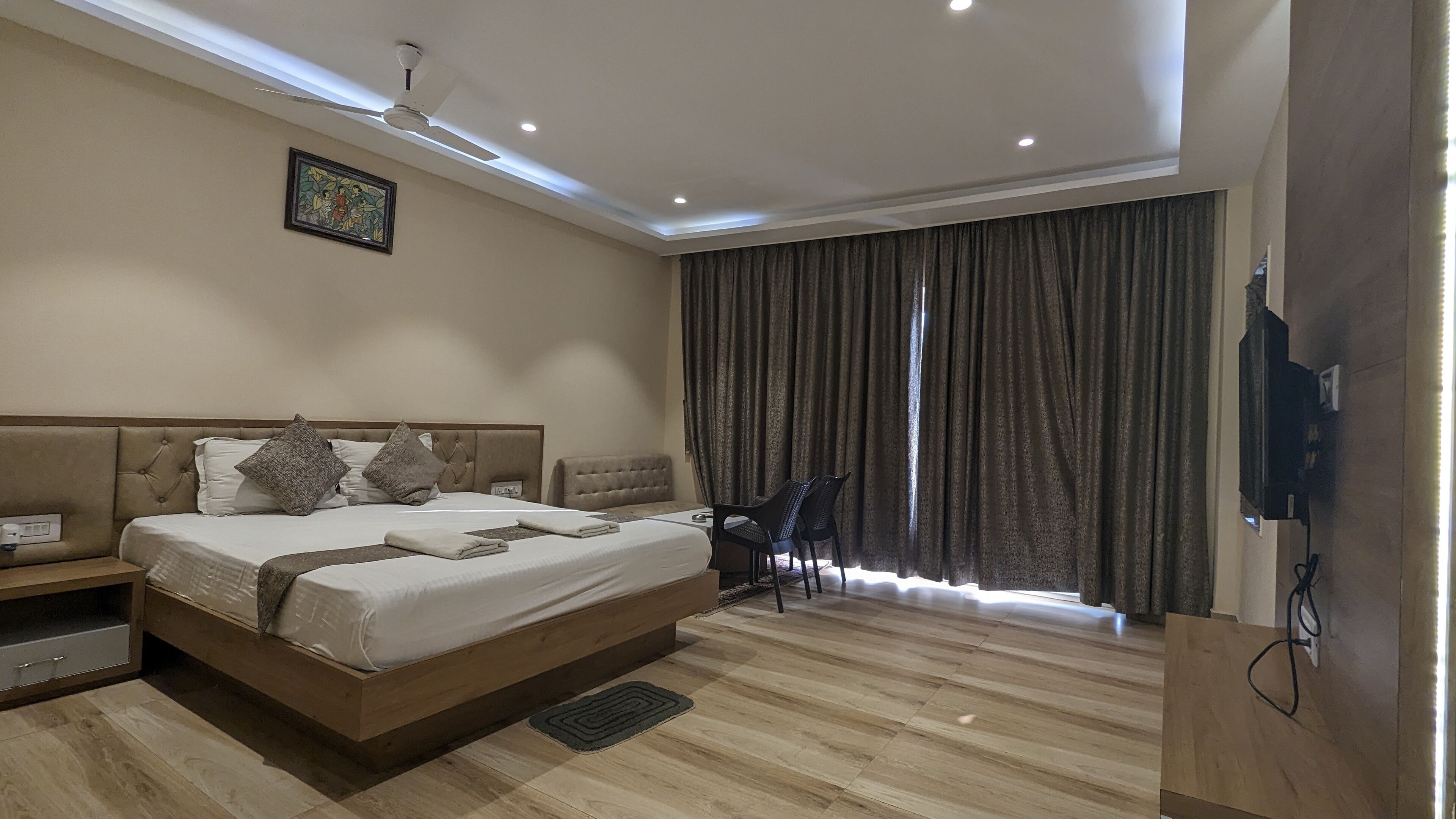 A hotel room with a large bed, a ceiling fan, a TV, and a window with curtains.