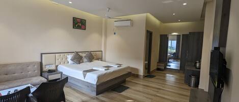 A modern bedroom with a large bed, a sofa, a chair, and a TV.