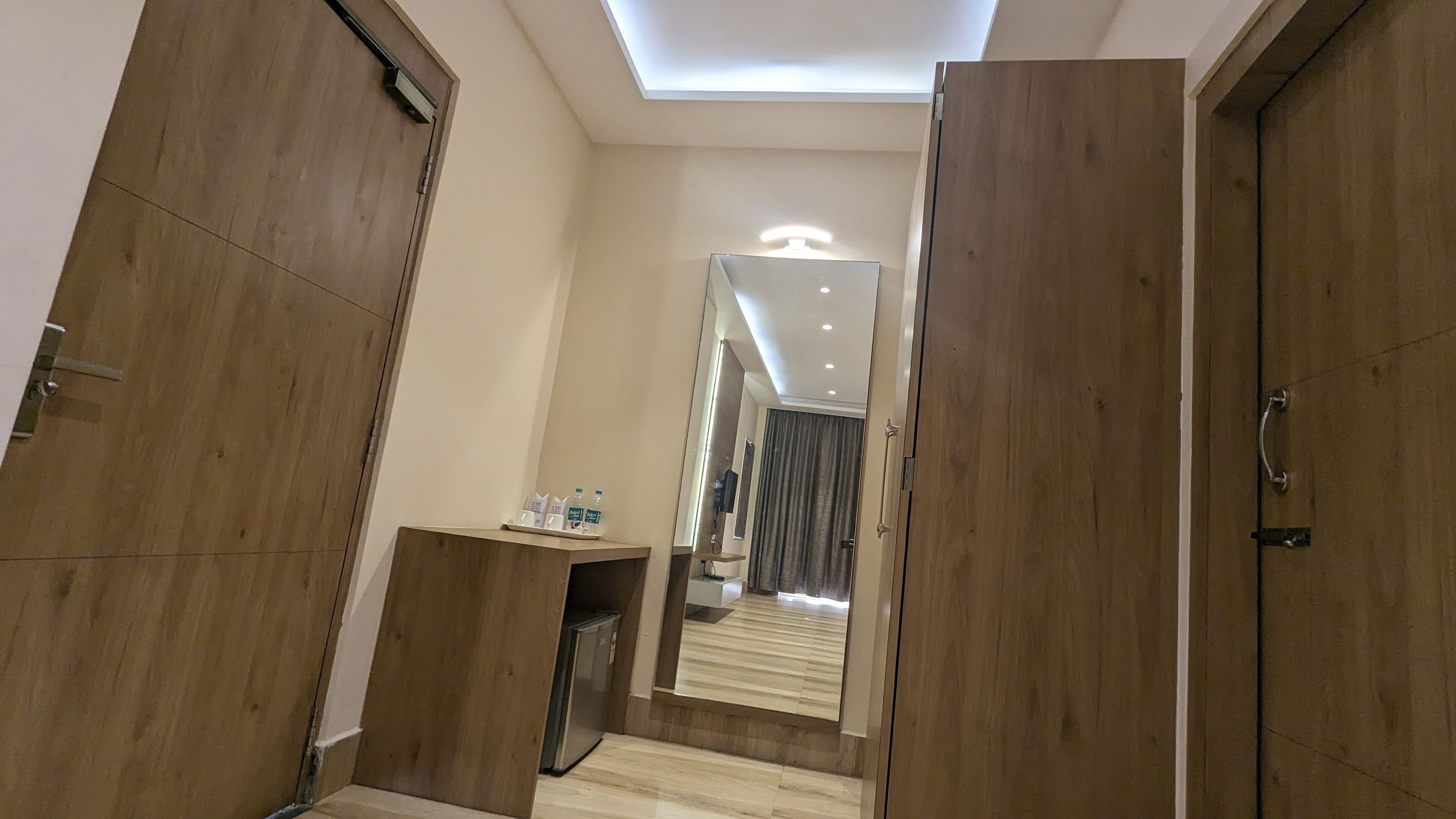 Een moderne hotelkamer met houten deuren, een spiegel, een bureau met toiletartikelen en een plafondlamp.