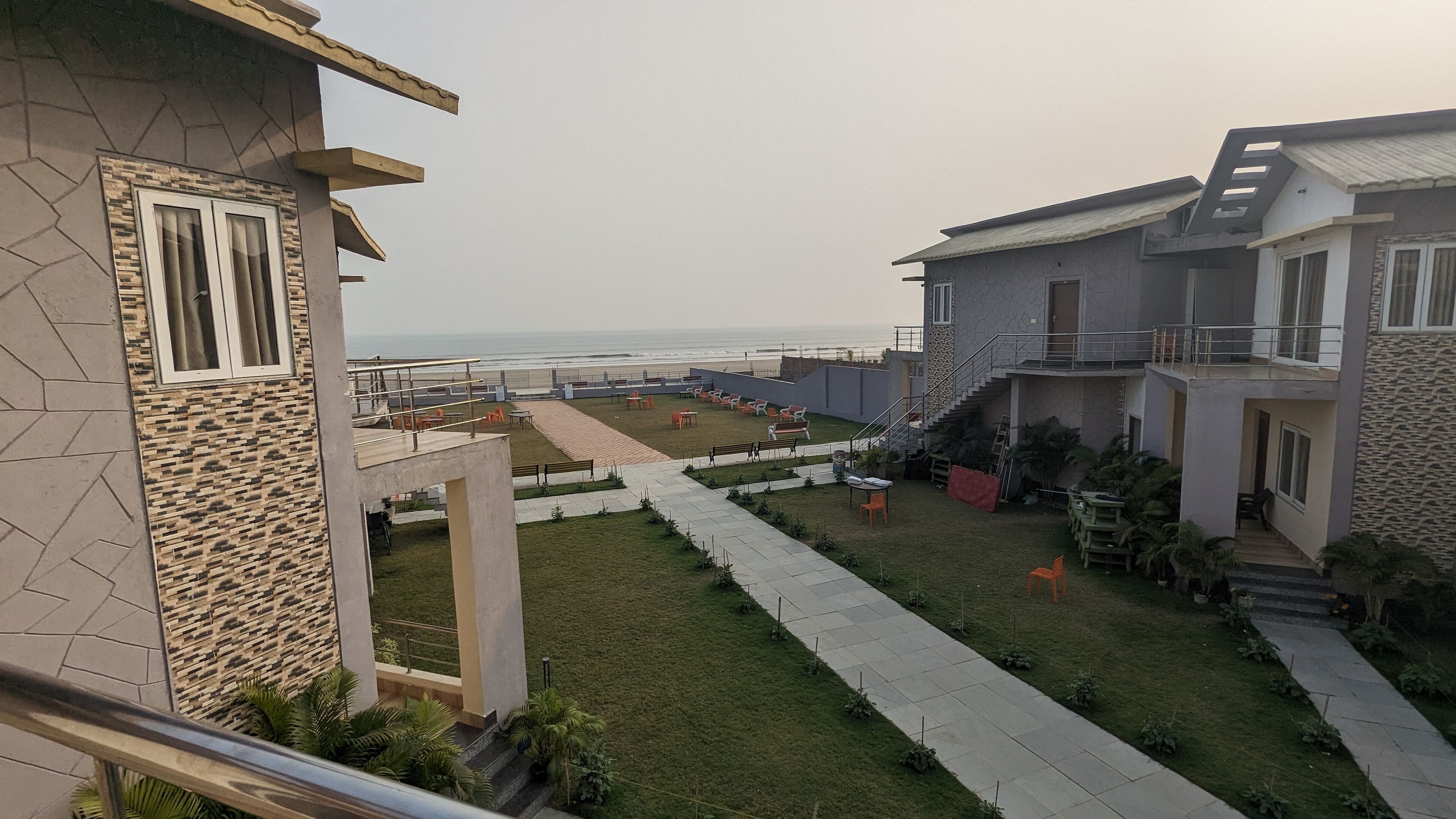 Pátio com vista para a praia, mobiliário ao ar livre e escada que dá acesso aos andares superiores.