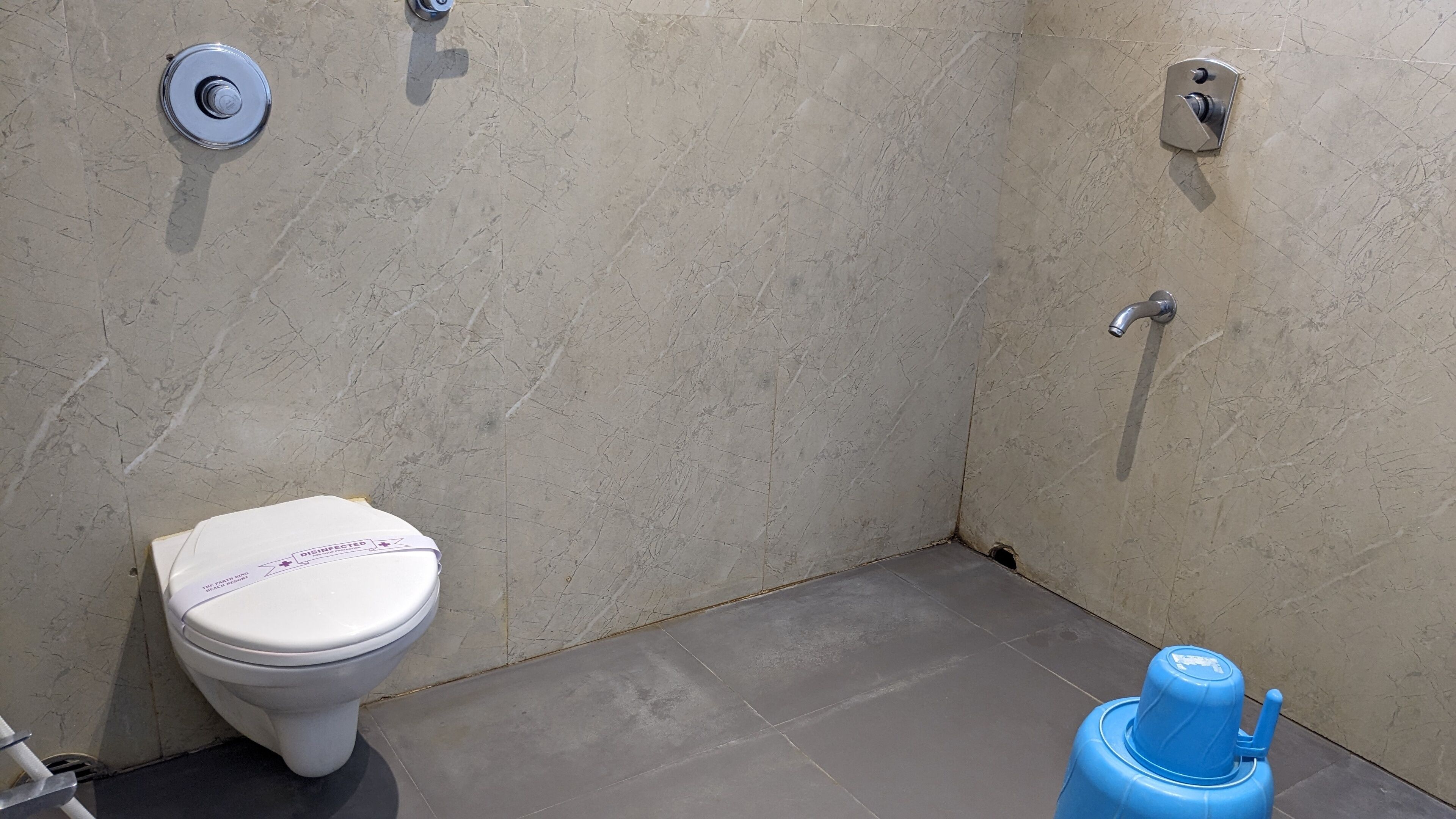 A small bathroom with a toilet, a blue hand dryer, and a wall-mounted faucet.