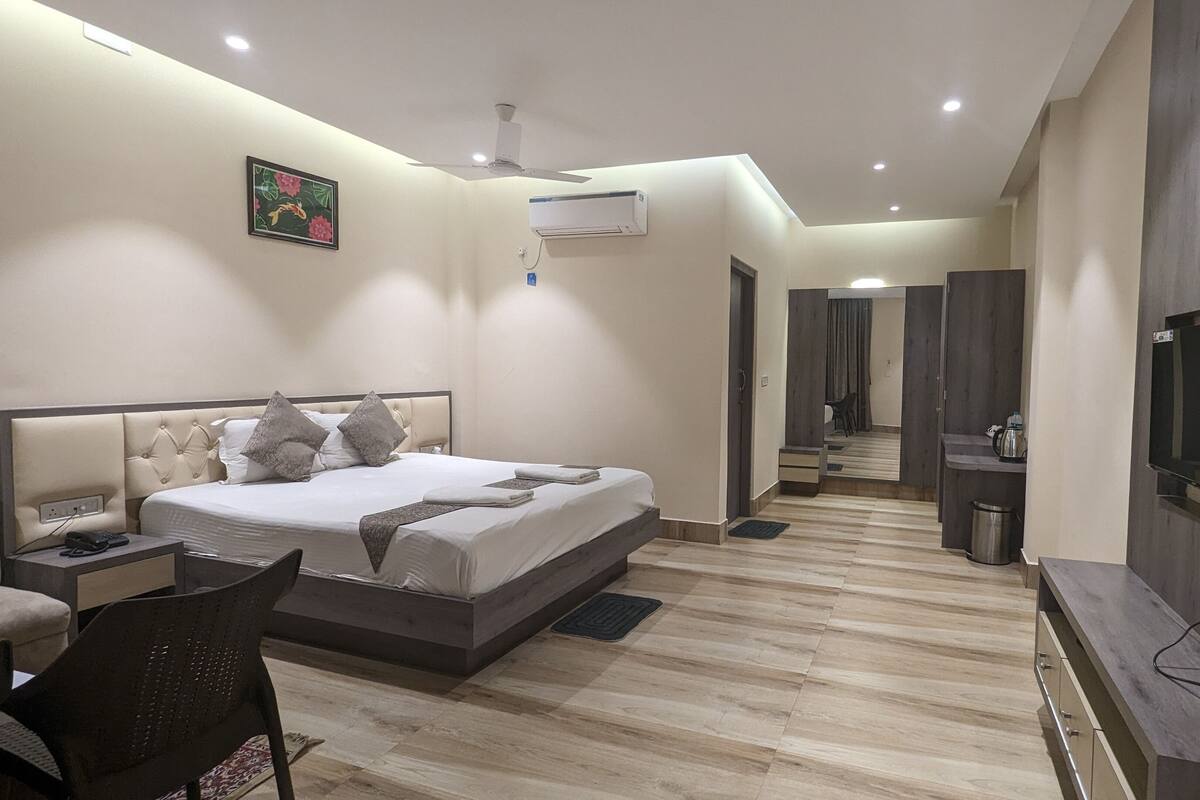 Una habitación de hotel moderna con una cama grande, mesita de noche, sillón y televisor montado en la pared.