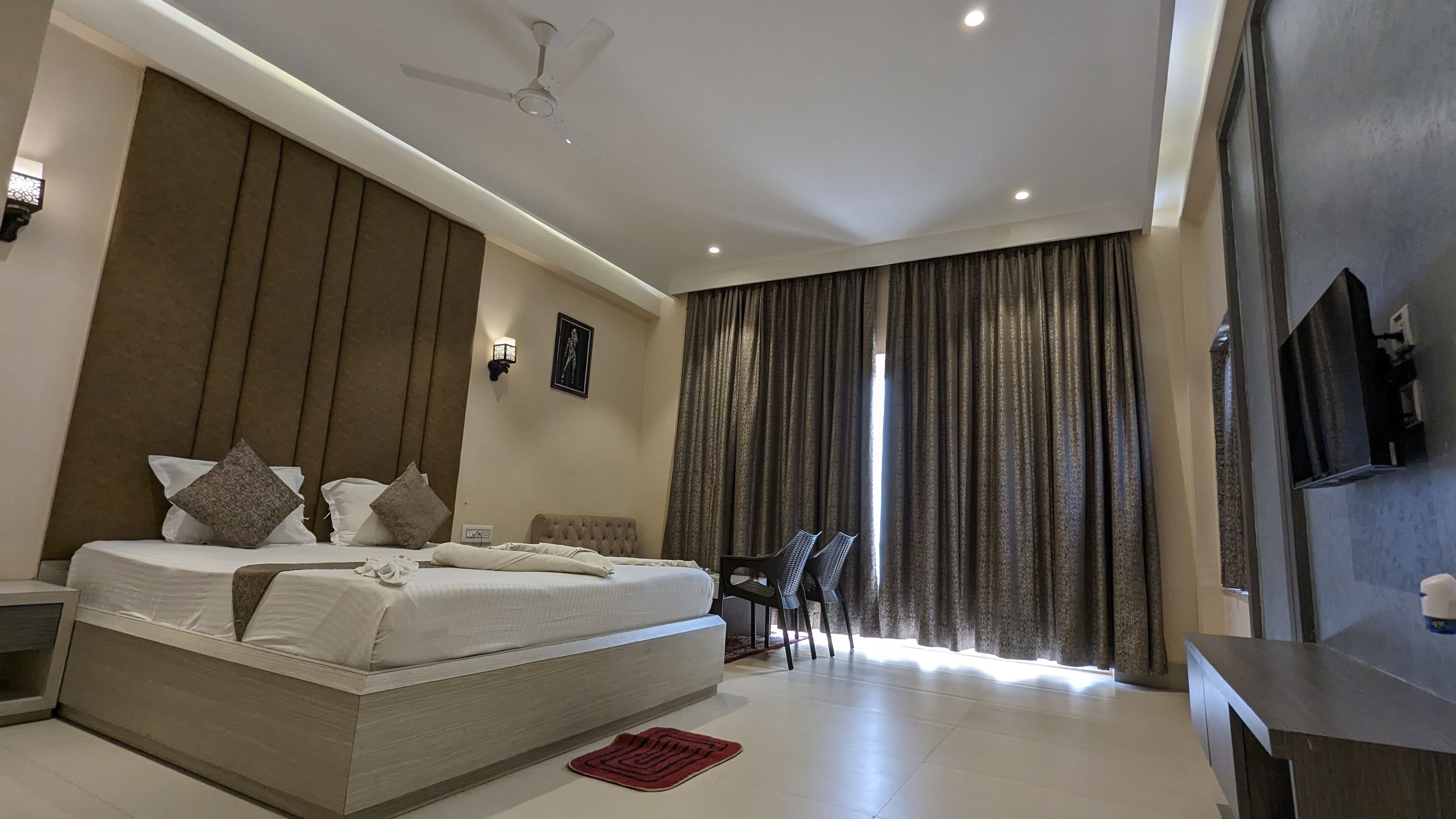 Een moderne hotelkamer met een groot bed, een plafondventilator, een televisie en een zithoek met stoelen.