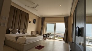 A spacious bedroom with a large bed, a ceiling fan, a TV, and a balcony with a view of the sea. - PARTH KING BEACH RESORT (Kanthi)