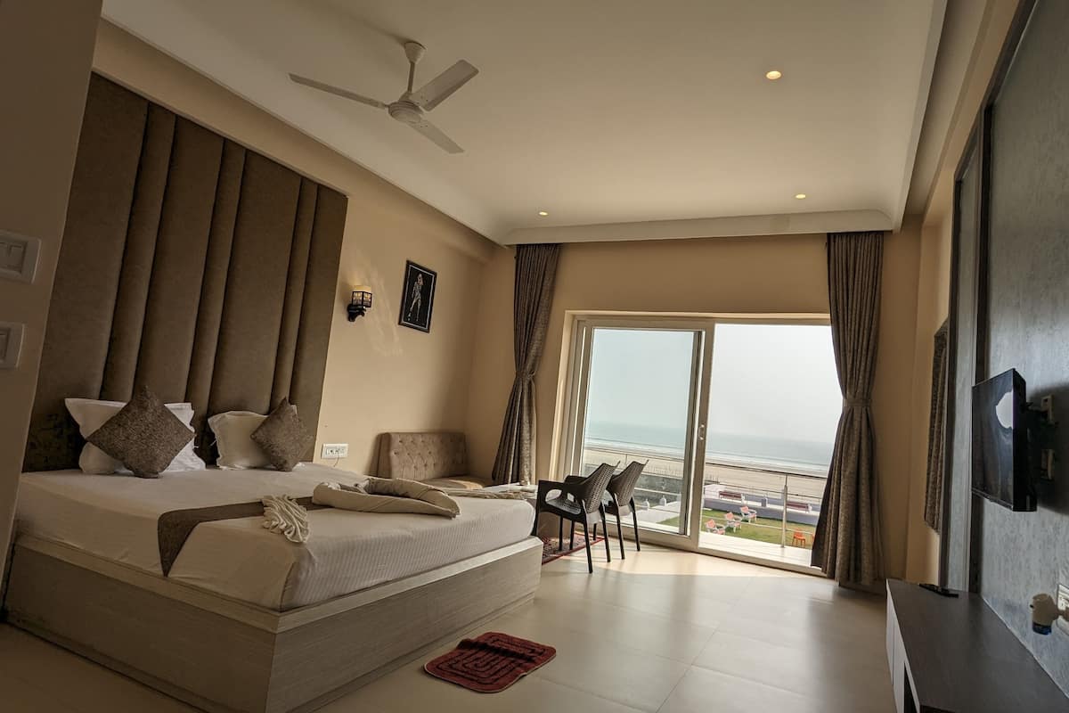 Un dormitorio espacioso con una cama grande, ventilador de techo, televisor y balcón con vista al mar.