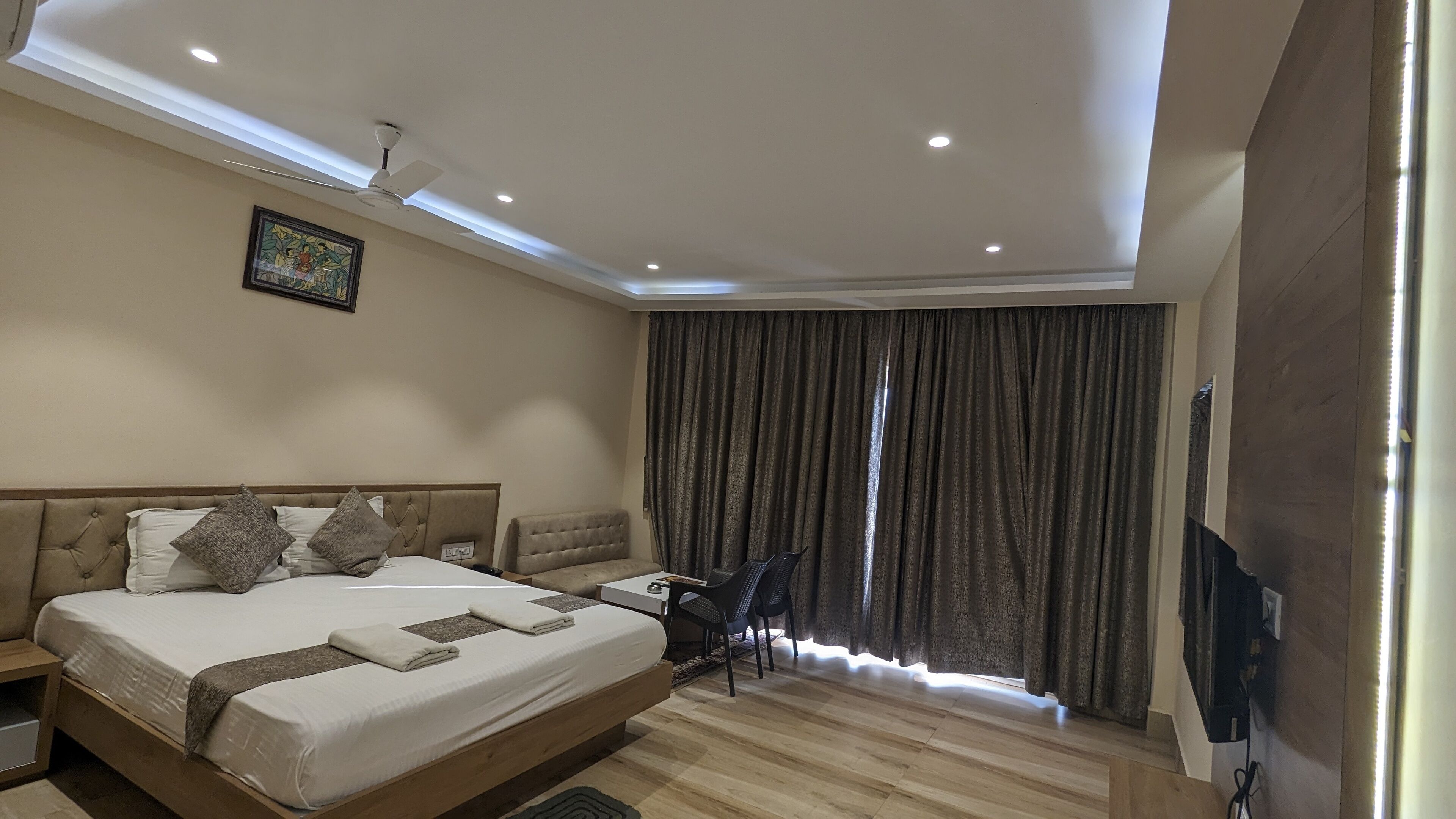 A modern hotel room with a large bed, a desk, a chair, and a ceiling fan.