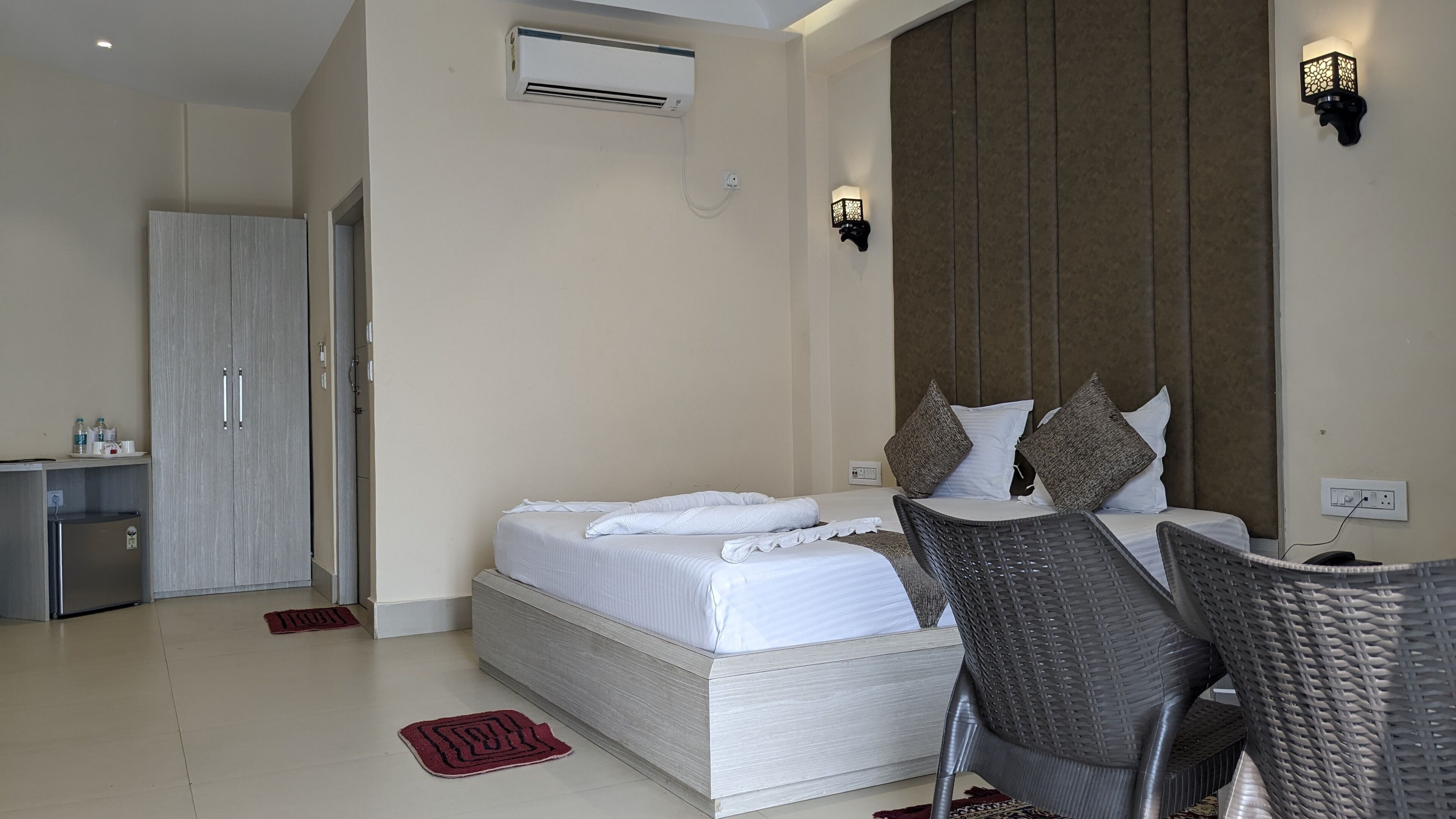 A bedroom with a bed, a chair, an air conditioning unit, and a wall-mounted light fixture.
