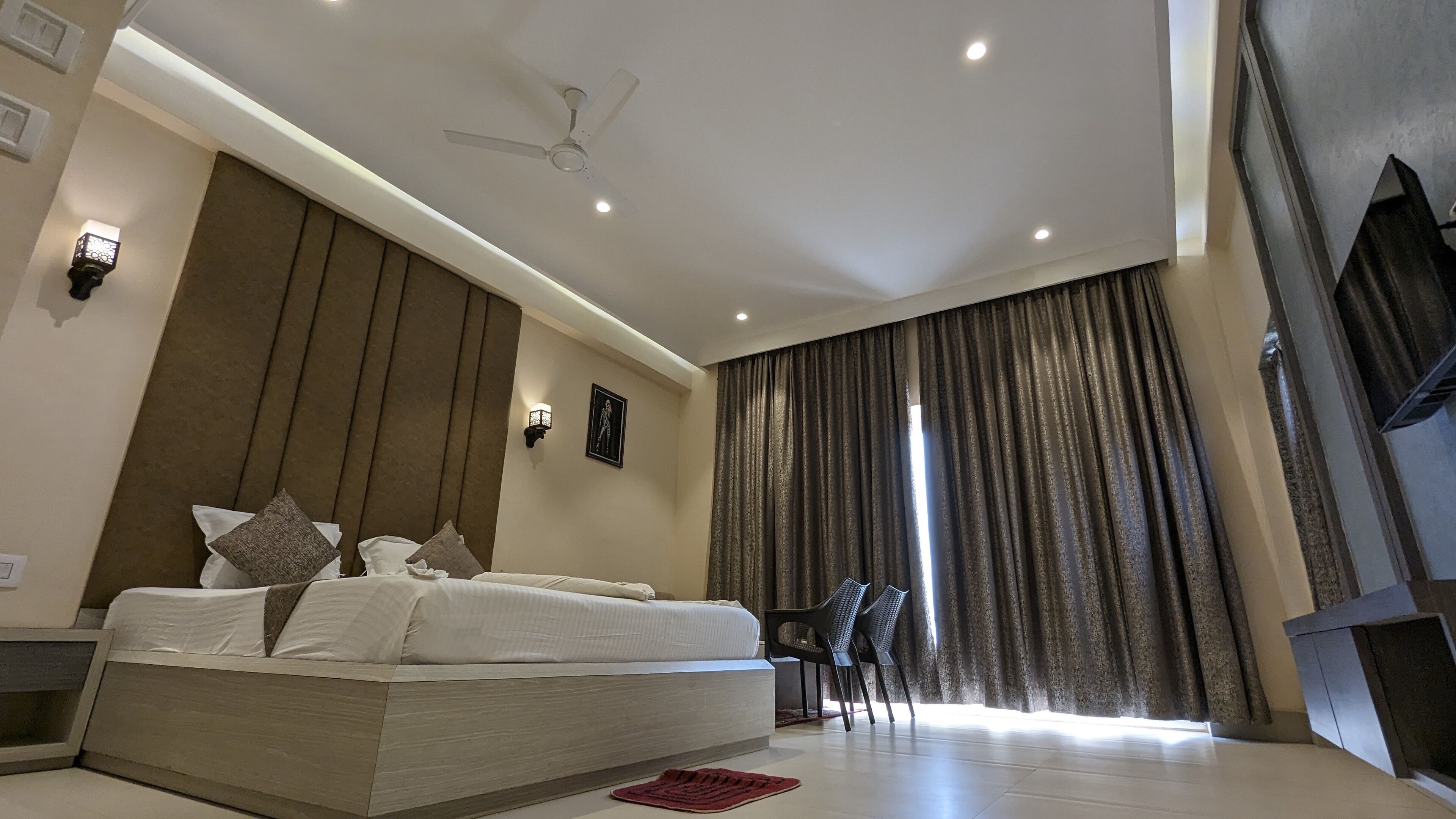 A modern bedroom with a large bed, a ceiling fan, and a view of the outdoors through a window with curtains.