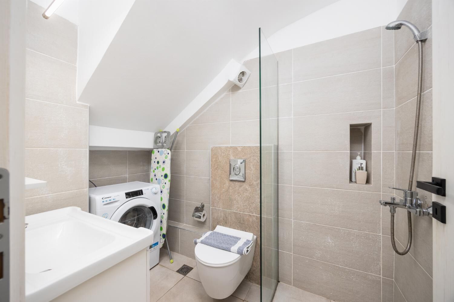 A modern bathroom with a washing machine, toilet, and shower.