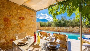 An outdoor dining area with stone walls, a pool, and a view of the mountains.