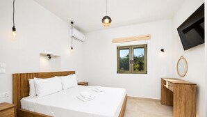 A modern bedroom with a wooden bed, bedside tables, a built-in desk, a flat-screen TV, and a window with a view of greenery.