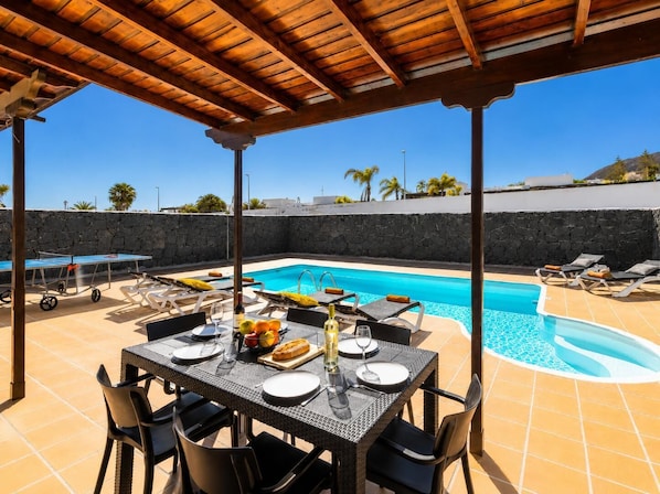 A poolside area with a table set for dining, lounge chairs, and a view of a swimming pool.