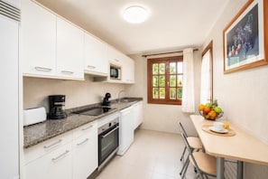 Eine Küche mit weißen Schränken, einer Mikrowelle, einer Kaffeemaschine und einem Essbereich mit Tisch und Stühlen.