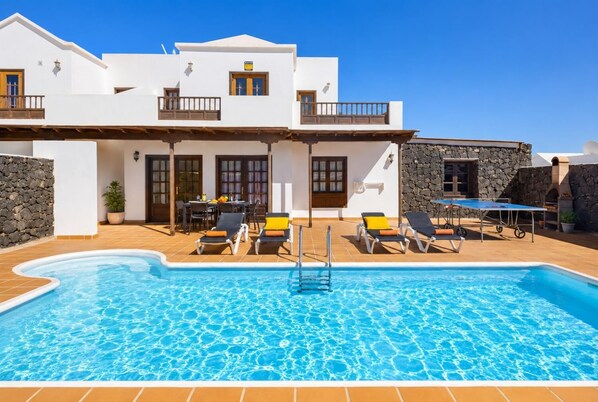 Un espace aménagé au bord de la piscine, avec une piscine à l’eau cristalline, des chaises longues et une table entourée de chaises.