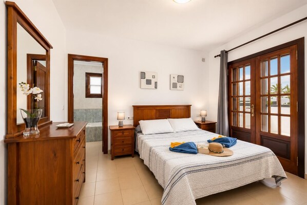 Ein Schlafzimmer mit Bett, Nachttischen, einem Schminktisch und einem Spiegel, mit Blick durch ein Fenster.
