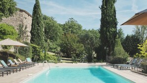 Una piscina con lettini e ombrelloni, immersa nel verde e circondata da un muro in pietra.